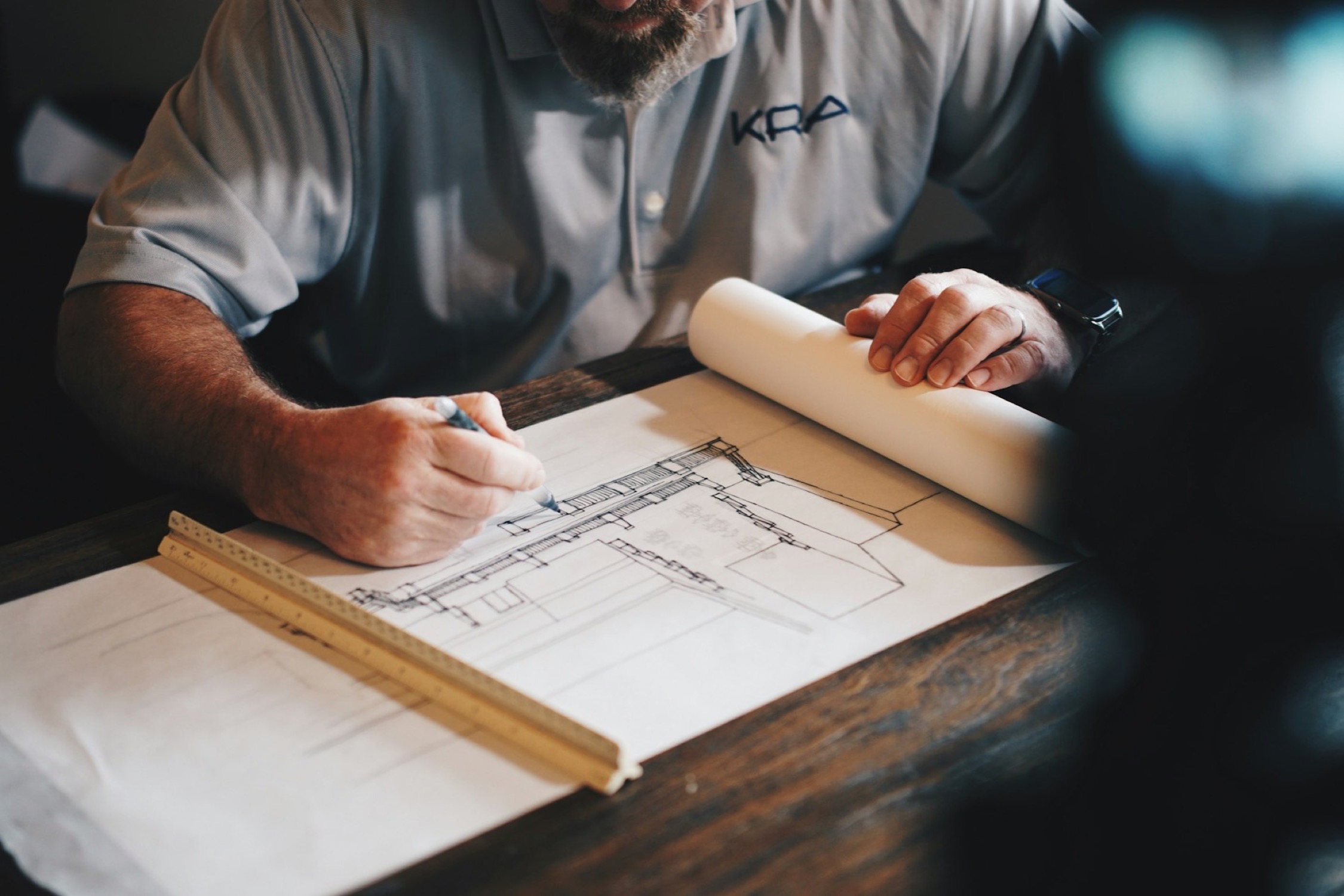A man marking up a technical drawing at a desk with a pencil and a ruler